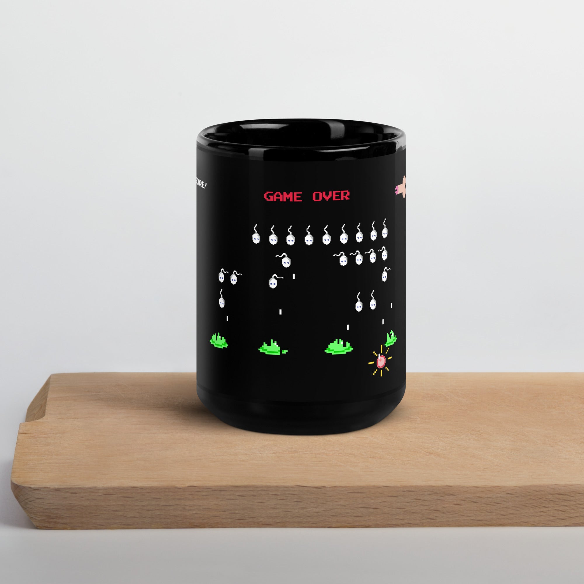 front facing glossy 15oz black mug  with Space Invaders parody illustration in the style of an 8 bit graphic. A penis spaceship fires sperms (aliens) who fire downward towards a human egg. A sperm has hit the egg and the text Game Over appears over the image